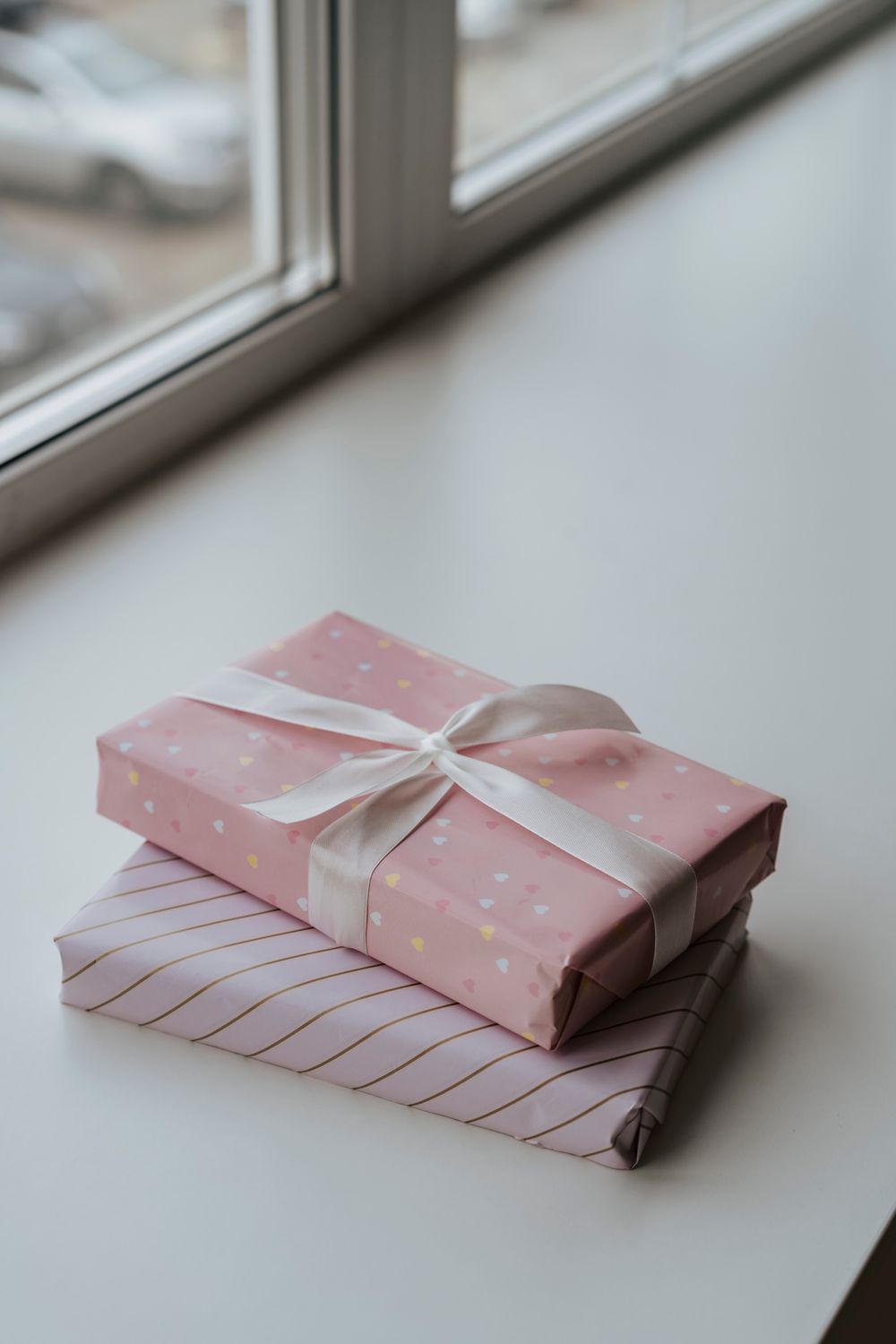 Twee in roze papier verpakte cadeautjes met een lint, in het licht van een raam.