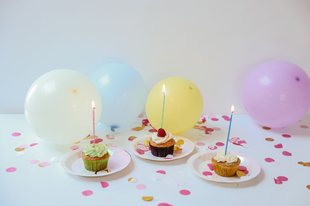 Cupcakes met brandende kaarsjes voor pastelkleurige ballonnen en confetti.