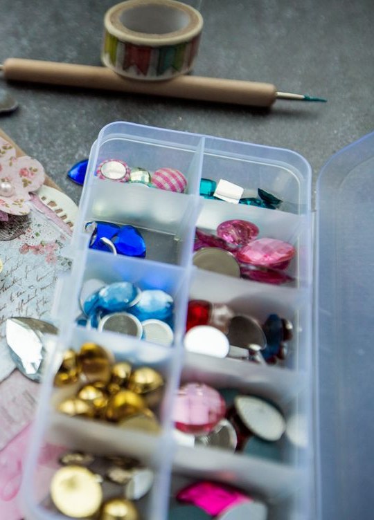 Sorteerbakje met gekleurde facetsteentjes in goud, roze en blauw, naast kant en washitape.