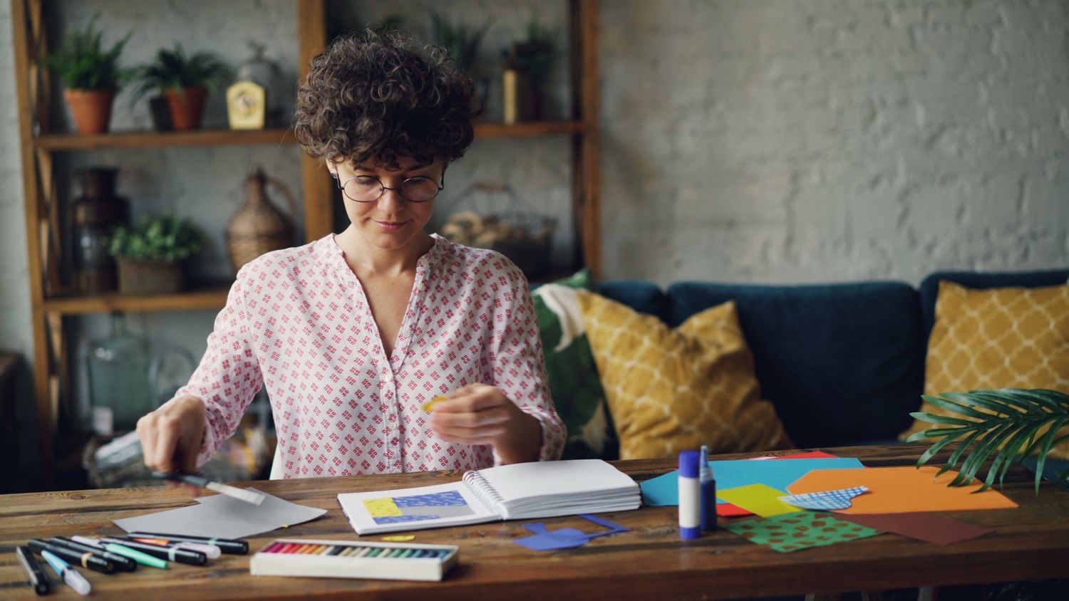Iemand werkt aan een grote werktafel met papier, lijm en stiften in een lichte werkruimte.